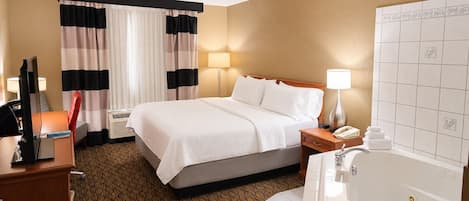 Habitación de hotel con cama, lámparas de noche, escritorio con teléfono y baño con bañera y lavamanos.