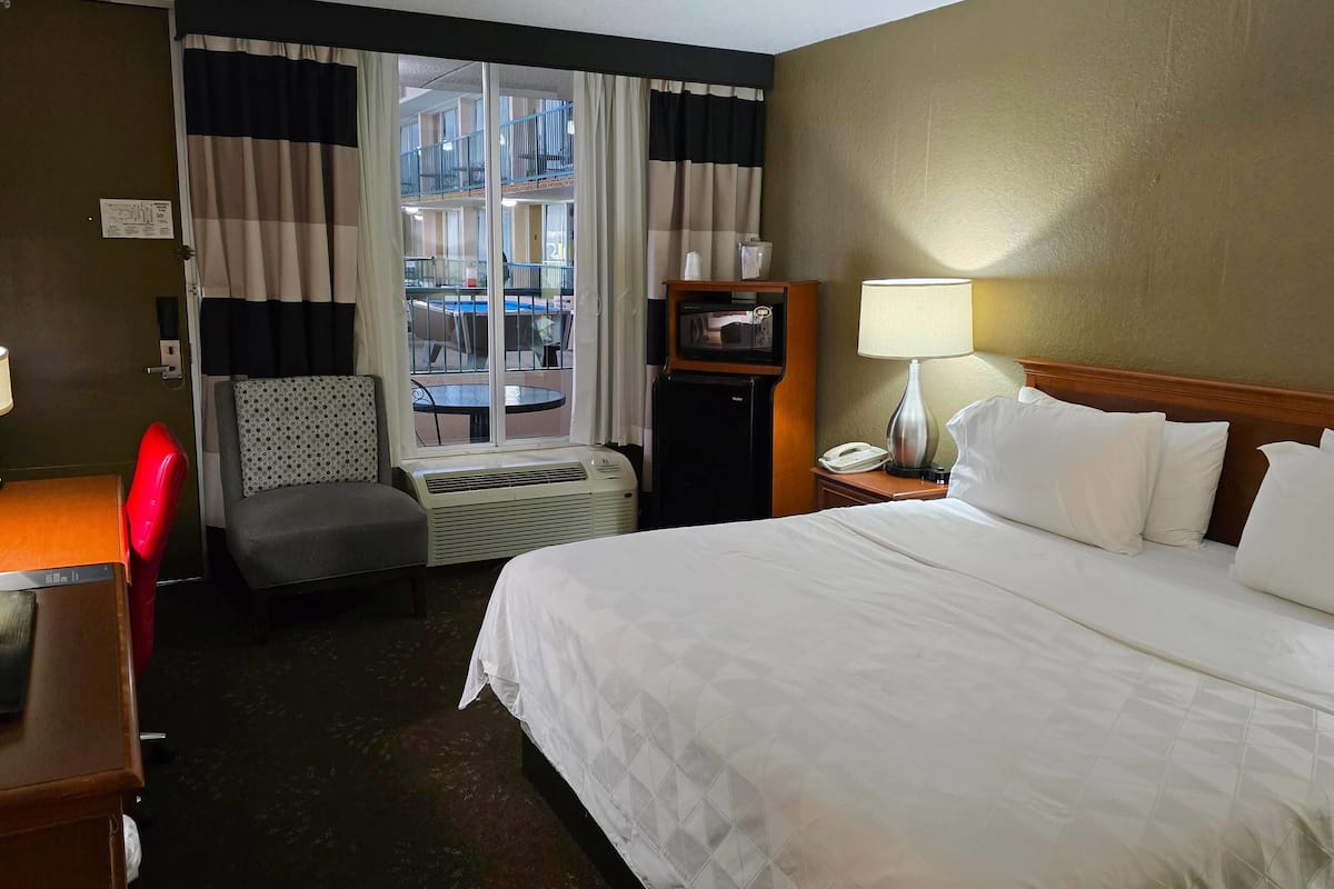 A hotel room with a bed, a desk, a chair, a TV, a lamp, and a window with curtains.