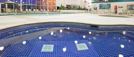Una piscina interior con suelo de baldosas azules, sillones de descanso y una zona de estar cubierta.