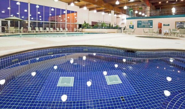 An indoor swimming pool with a blue tiled floor, lounge chairs, and a covered seating area. - Alexandria Hotel & Conference Center (Alexandria)