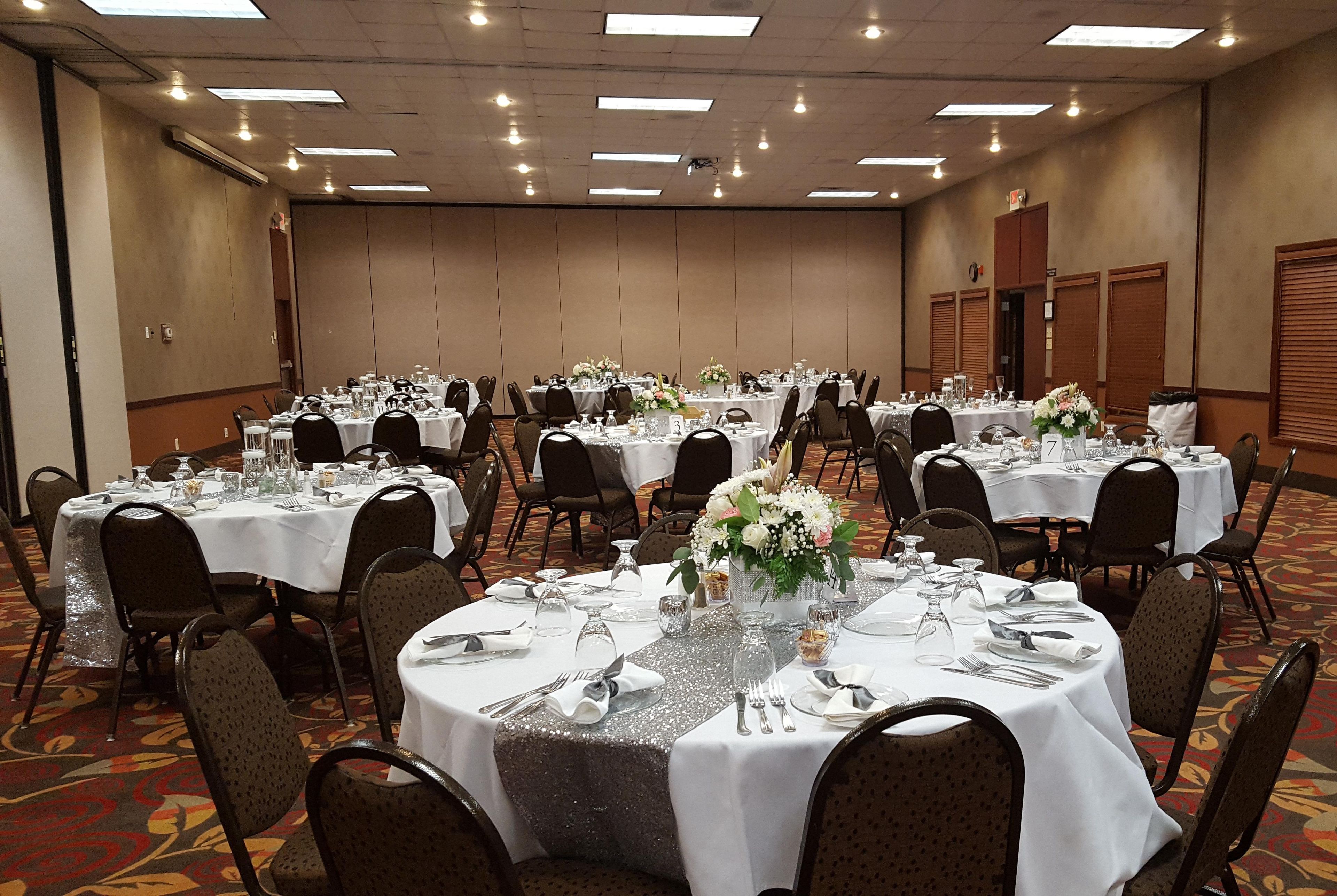 A banquet hall with round tables, chairs, and floral centerpieces.