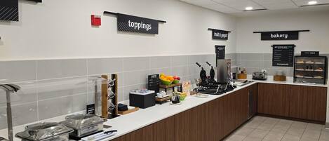 A self-service breakfast area with labeled sections for toppings, fruit & yogurt, and bakery.