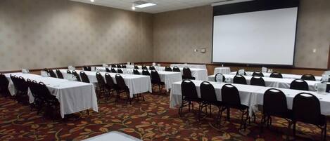A conference room with multiple tables and chairs, a projector screen, and a carpeted floor.