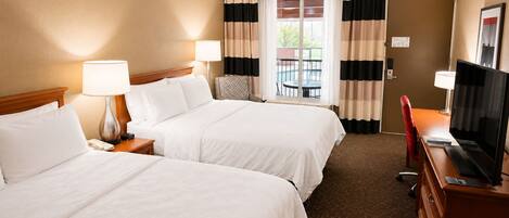 A hotel room with two beds, a desk with a TV, a chair, and a window with curtains.