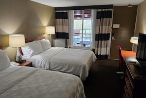 A hotel room with two beds, a desk, a chair, a lamp, and a view of the outdoors. - Alexandria Hotel & Conference Center (Alexandria)