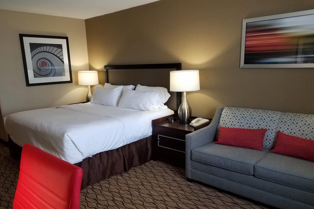 A hotel room with a bed, two bedside tables, a sofa, and a chair.