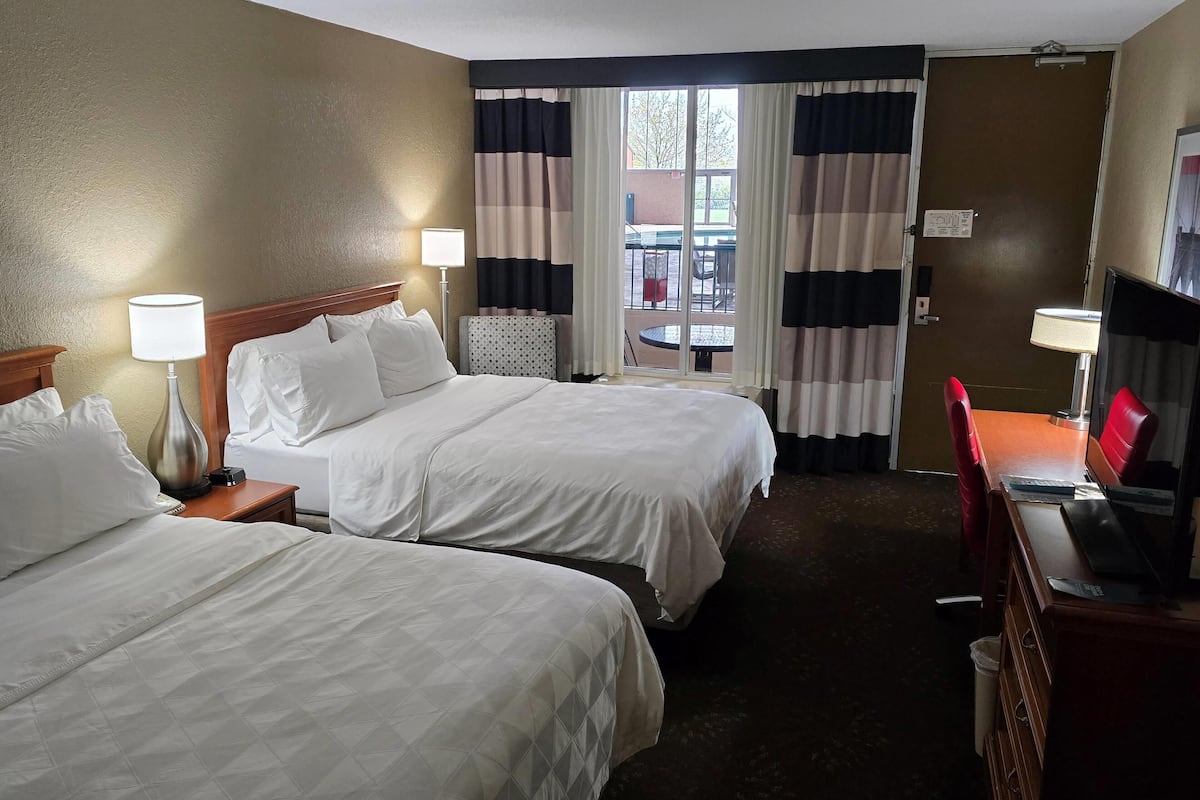 A hotel room with two beds, a desk with a computer, and a view of the outside.