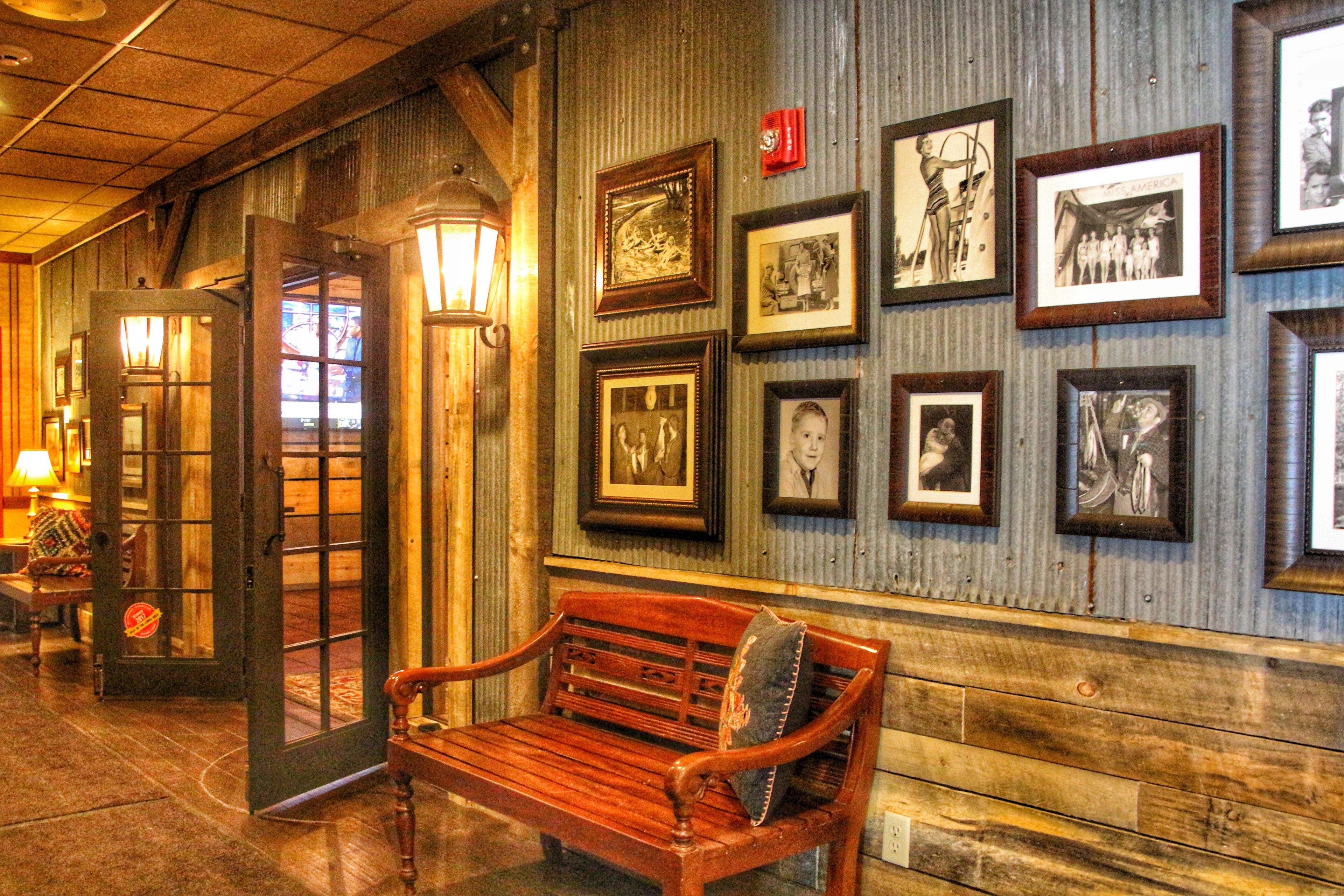 Un pasillo con un banco de madera, cuadros en la pared y una puerta con espejo.