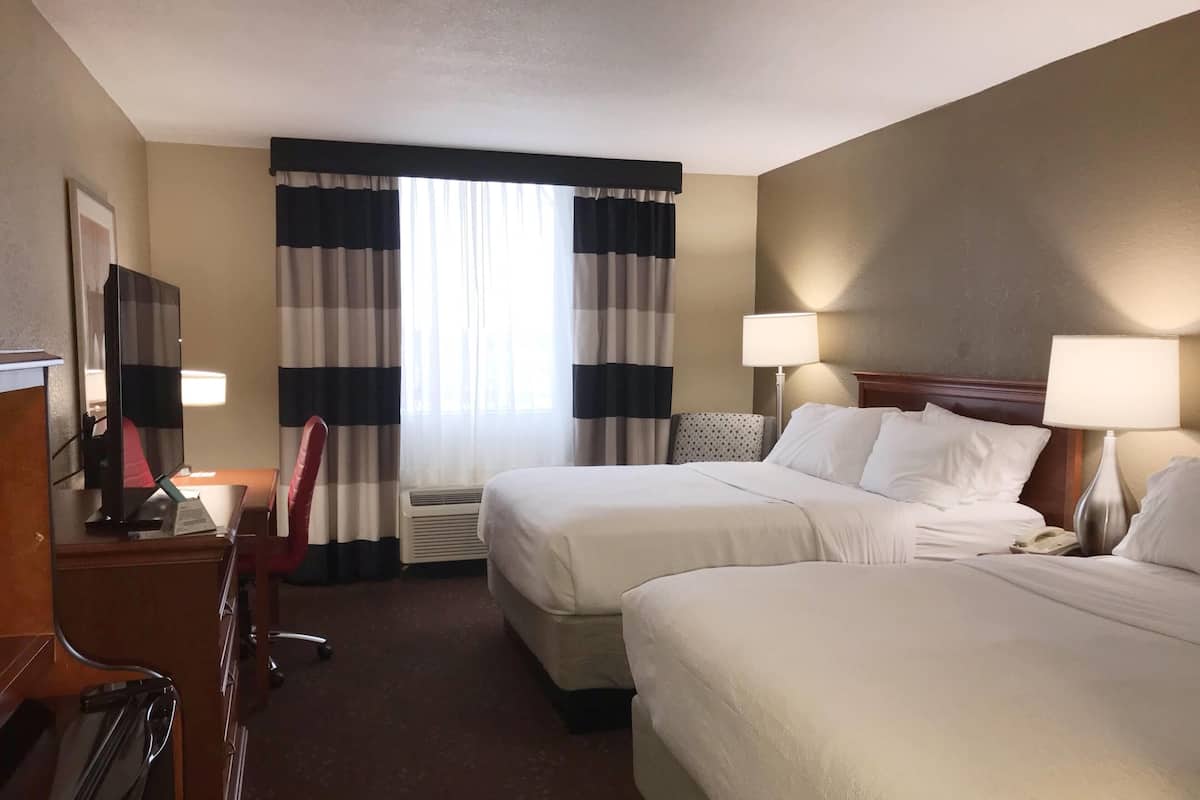 A hotel room with two beds, a desk with a computer, a chair, and two lamps.