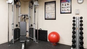 A gym with weightlifting equipment, a red exercise ball, and a wall-mounted dumbbell rack.