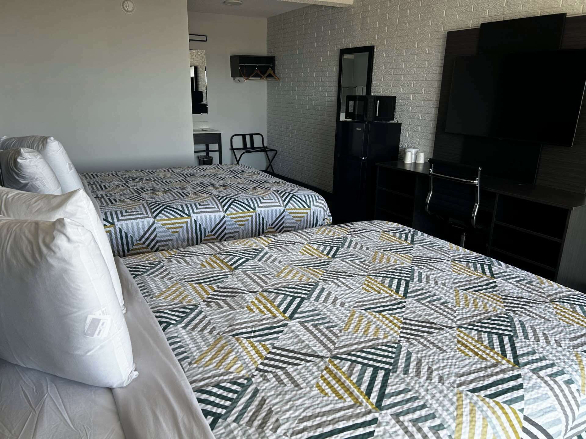 A hotel room with two beds, a TV, a mirror, and a small desk.