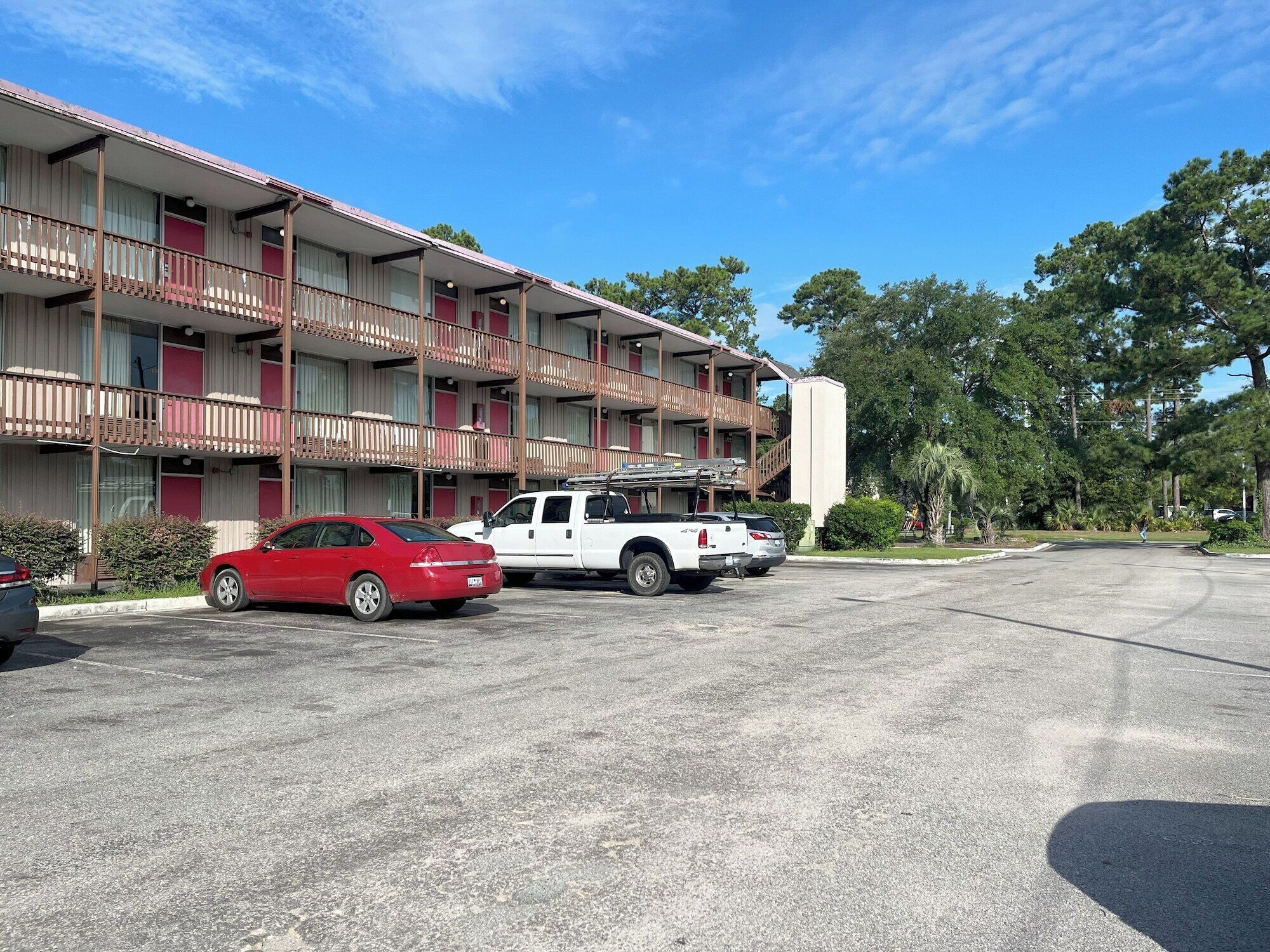 A multi-story motel with balconies, a parking lot, and a white pickup truck.