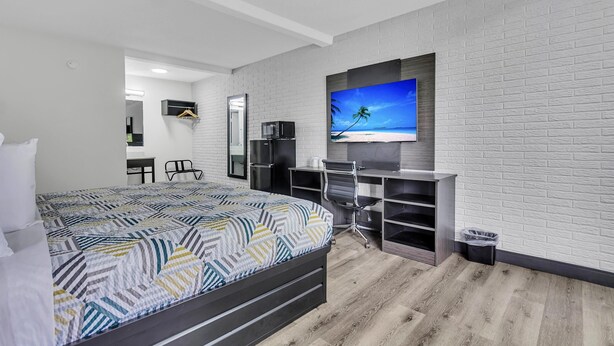 A modern hotel room with a large bed, a desk with a computer, a TV mounted on the wall, and a small trash bin.