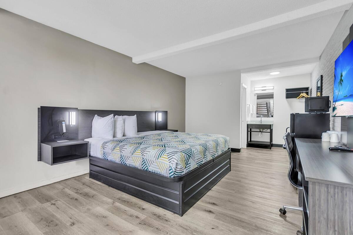 A modern hotel room with a bed, bedside table, and a desk with a chair.
