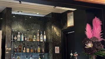 Zona bar con scaffali di bottiglie di liquore, un bancone e un'elegante composizione floreale rosa.