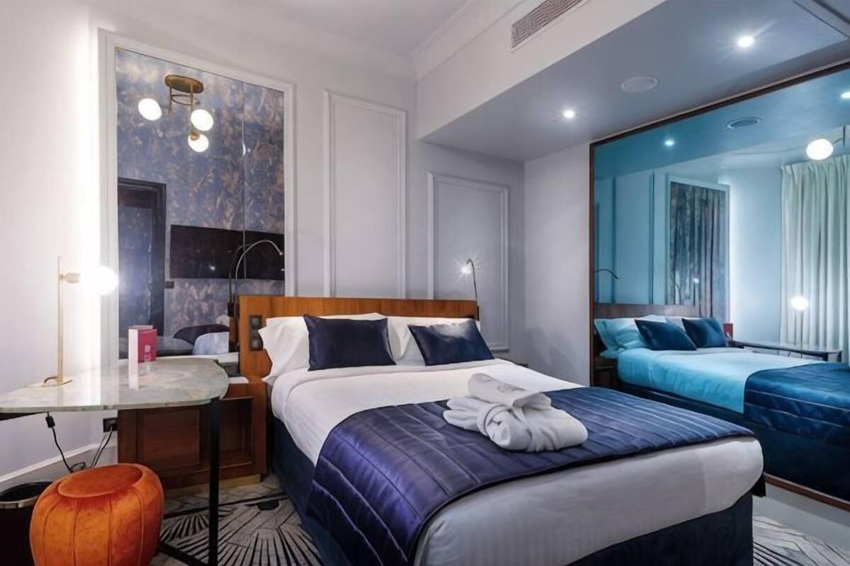 A hotel room with a large bed, a desk, a mirror, and a seating area.