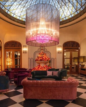 A luxurious lobby with a checkered floor, a large chandelier, and a decorative floral arrangement.