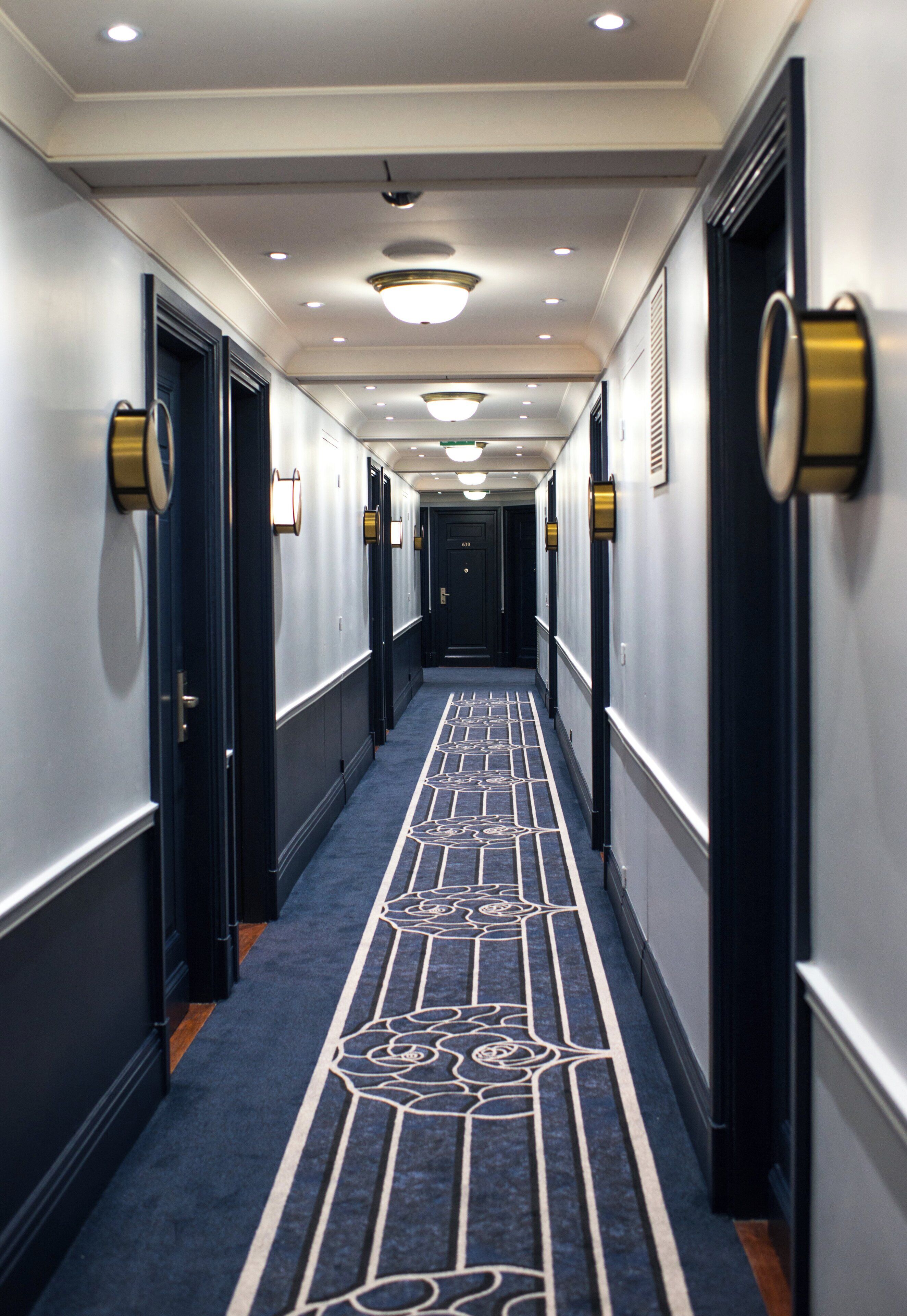 A hotel hallway with a patterned carpet, doors with round gold handles, and recessed lighting.
