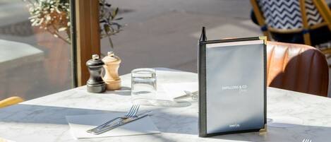 An outdoor dining area with a table set for two, a menu, salt and pepper shakers, and a small potted plant.