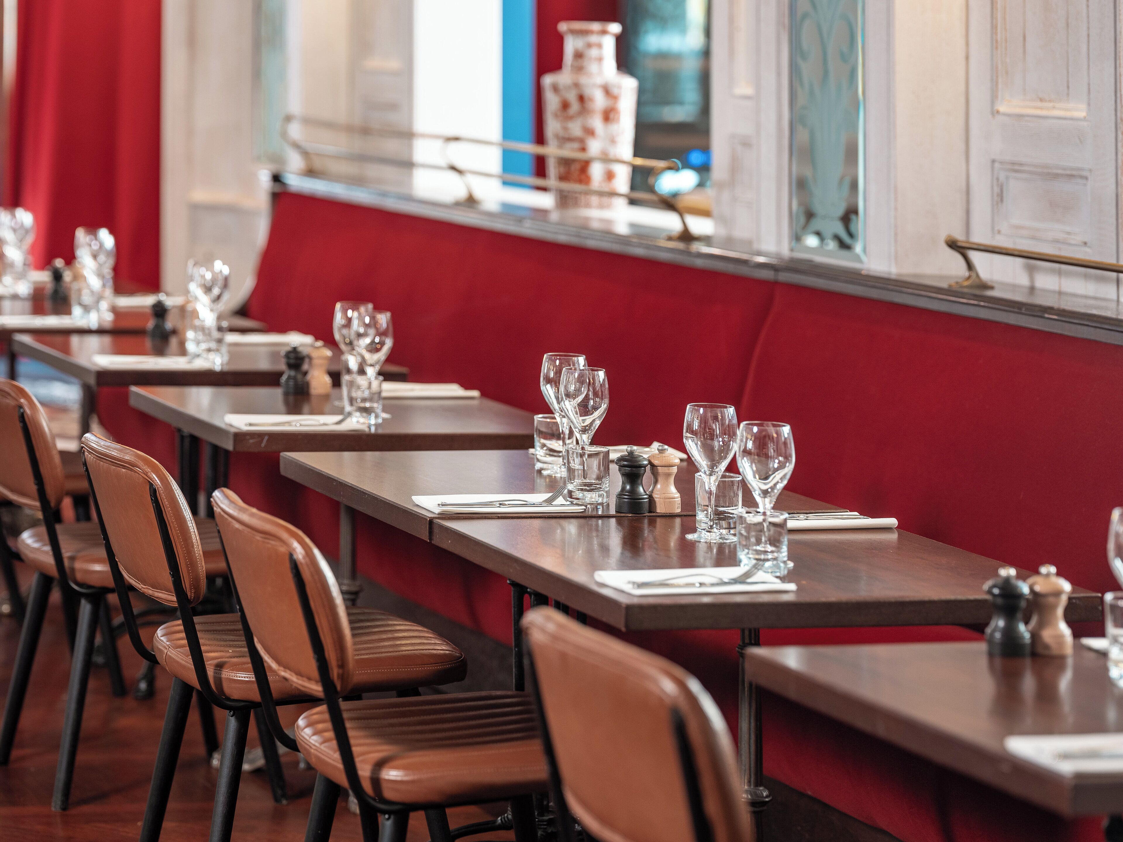 A restaurant with long wooden tables, brown leather chairs, and red cushioned benches.