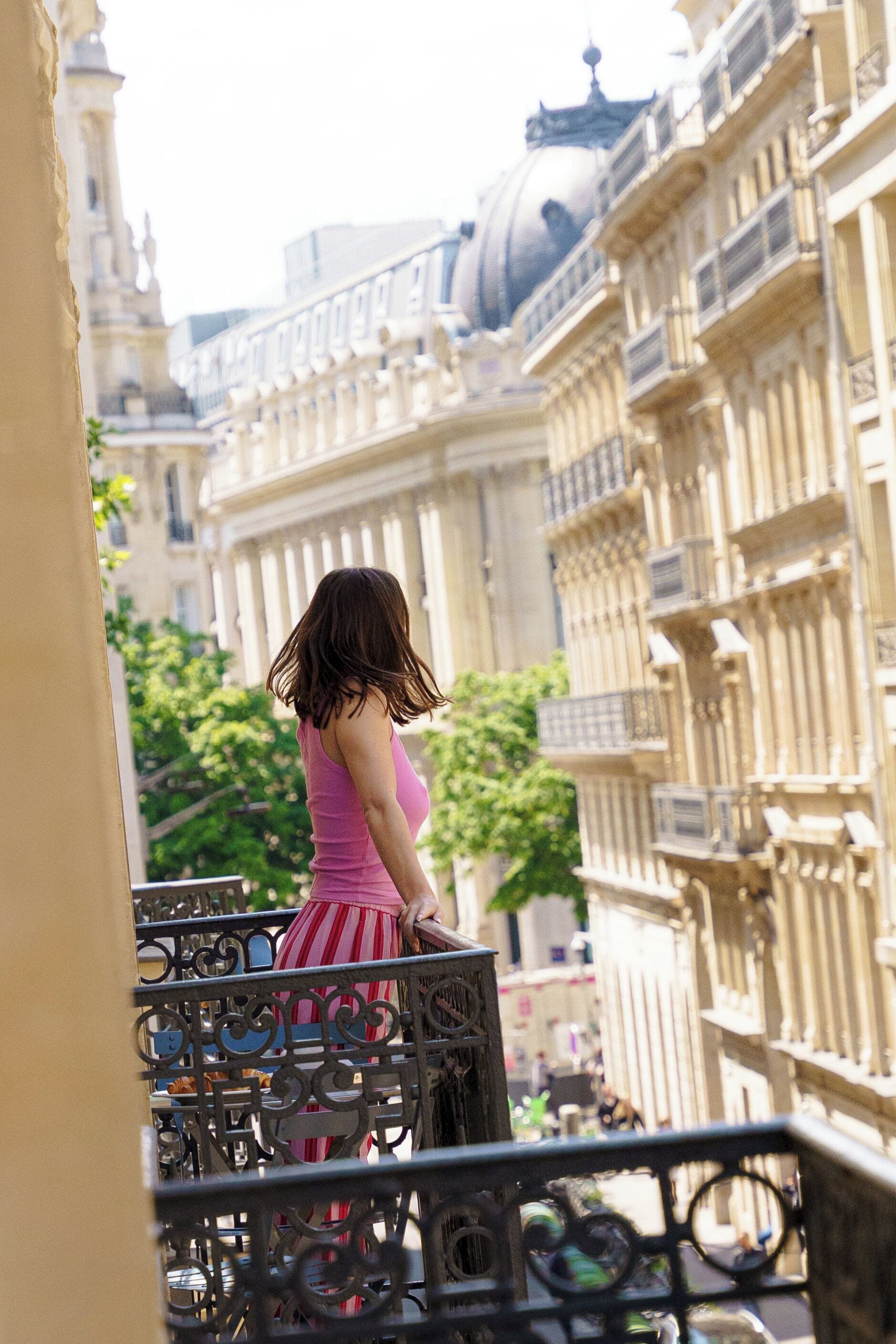 A woman on a balcony overlooking a cityscape with historic buildings.