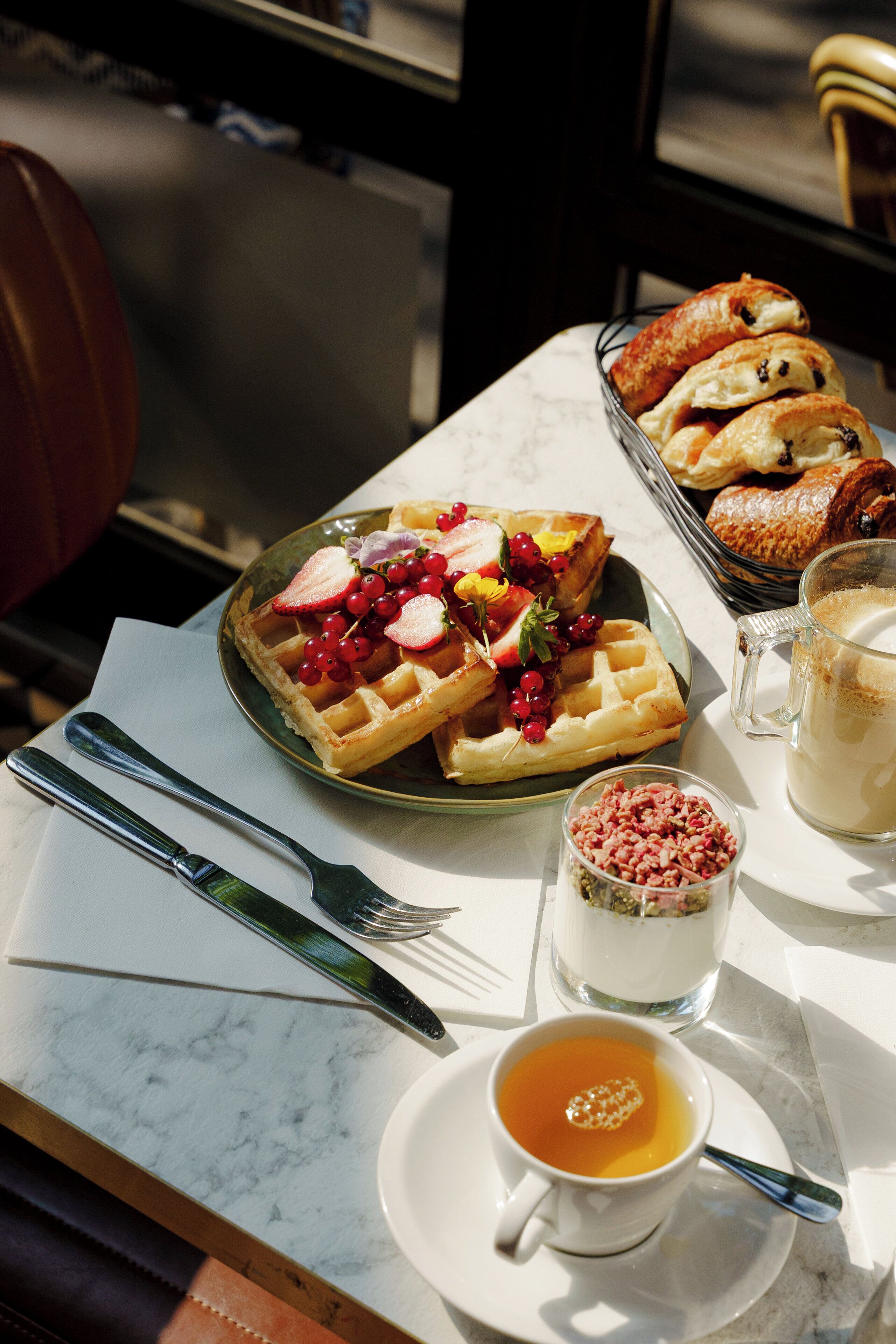 A breakfast setting with waffles topped with berries, a cup of tea, and a glass of milk on a marble table.