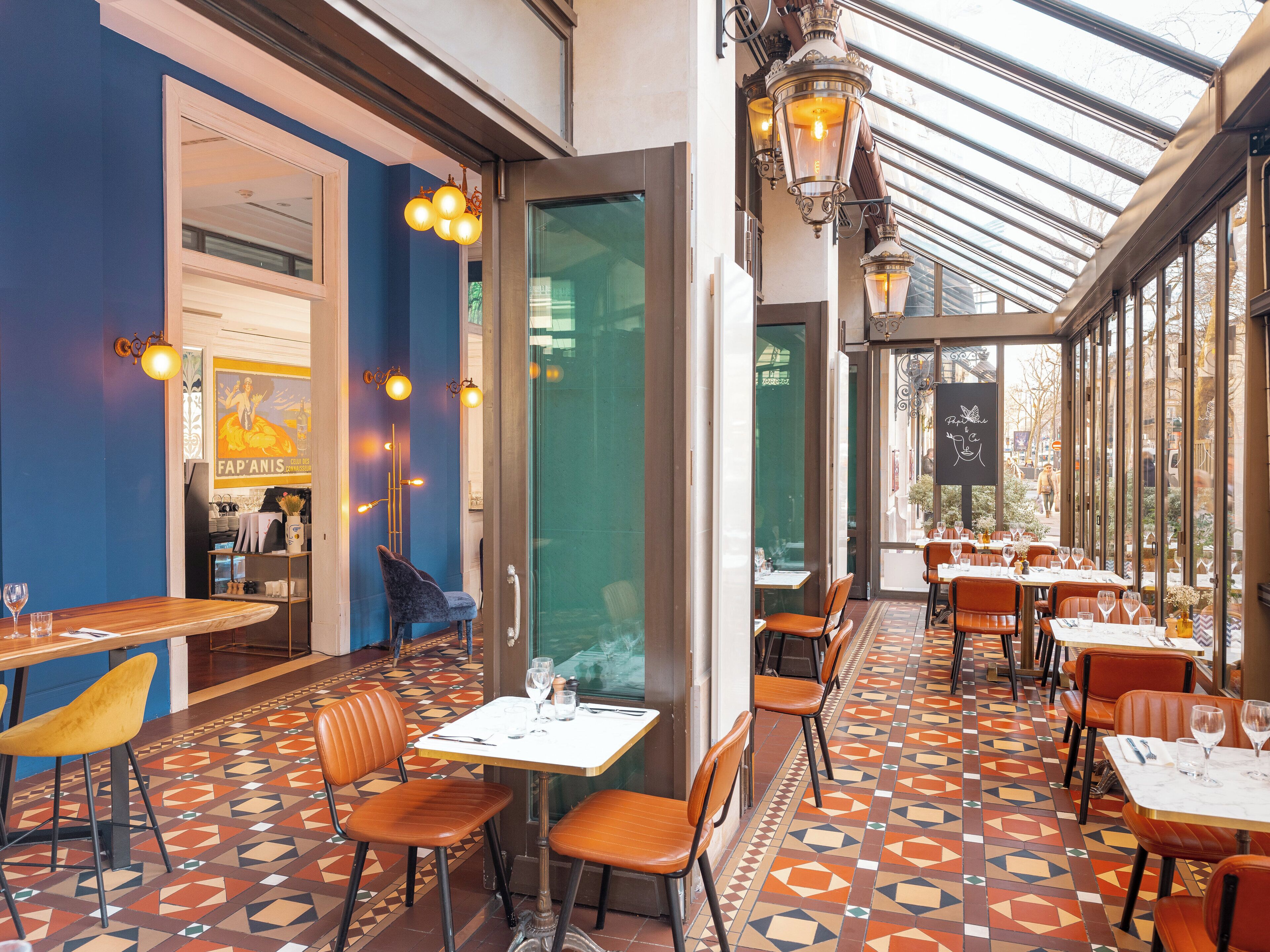 A restaurant with a geometric patterned floor, tables with chairs, and hanging light fixtures.