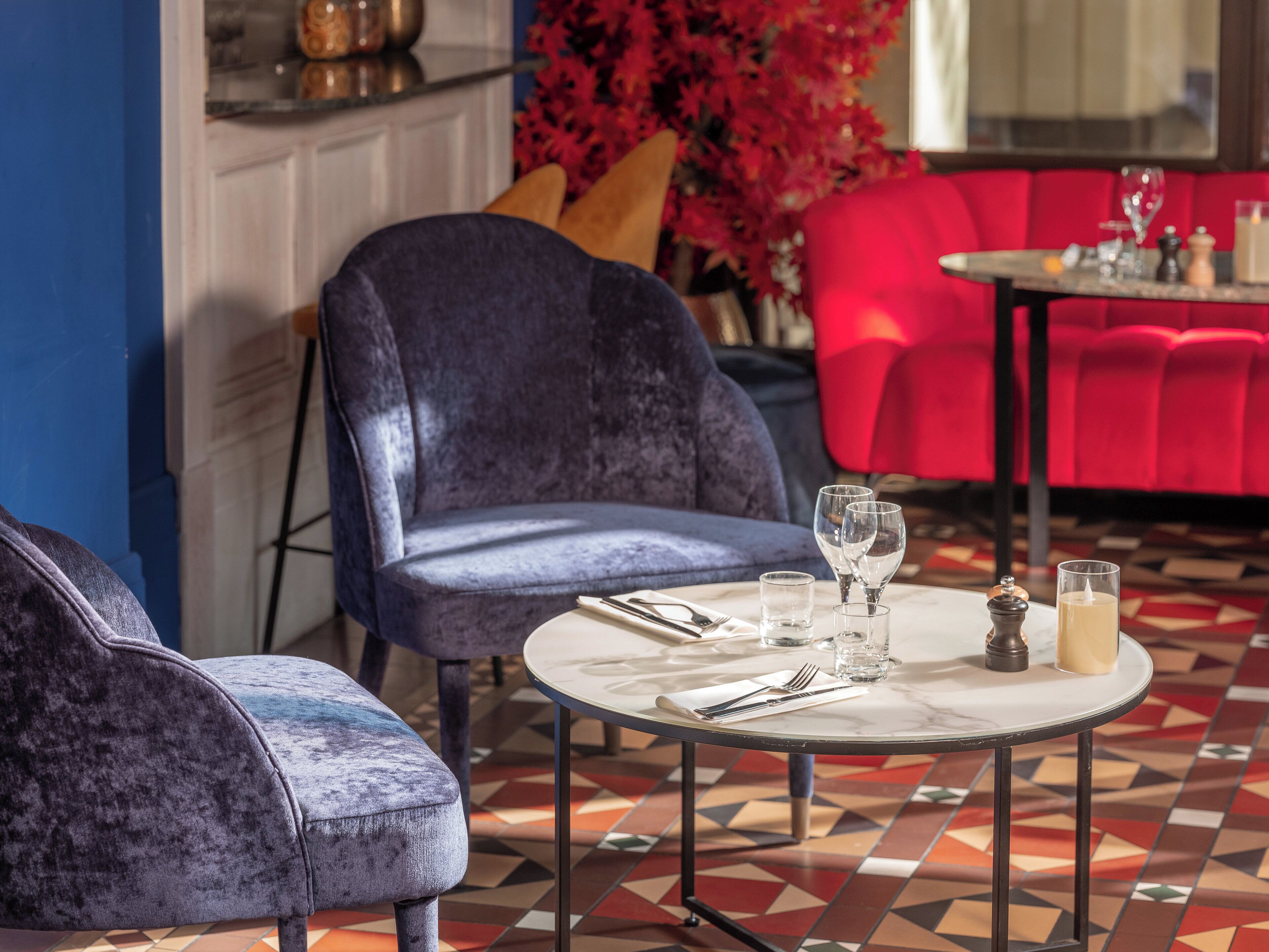 Un intérieur moderne avec une table ronde dressée pour le repas, une chaise bleue rembourrée et un canapé rouge.