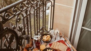 A balcony with a table set for breakfast, including croissants, bread, and fruit. A view of a building with multiple windows is visible in the background. - M Social Hotel Paris (Paris)