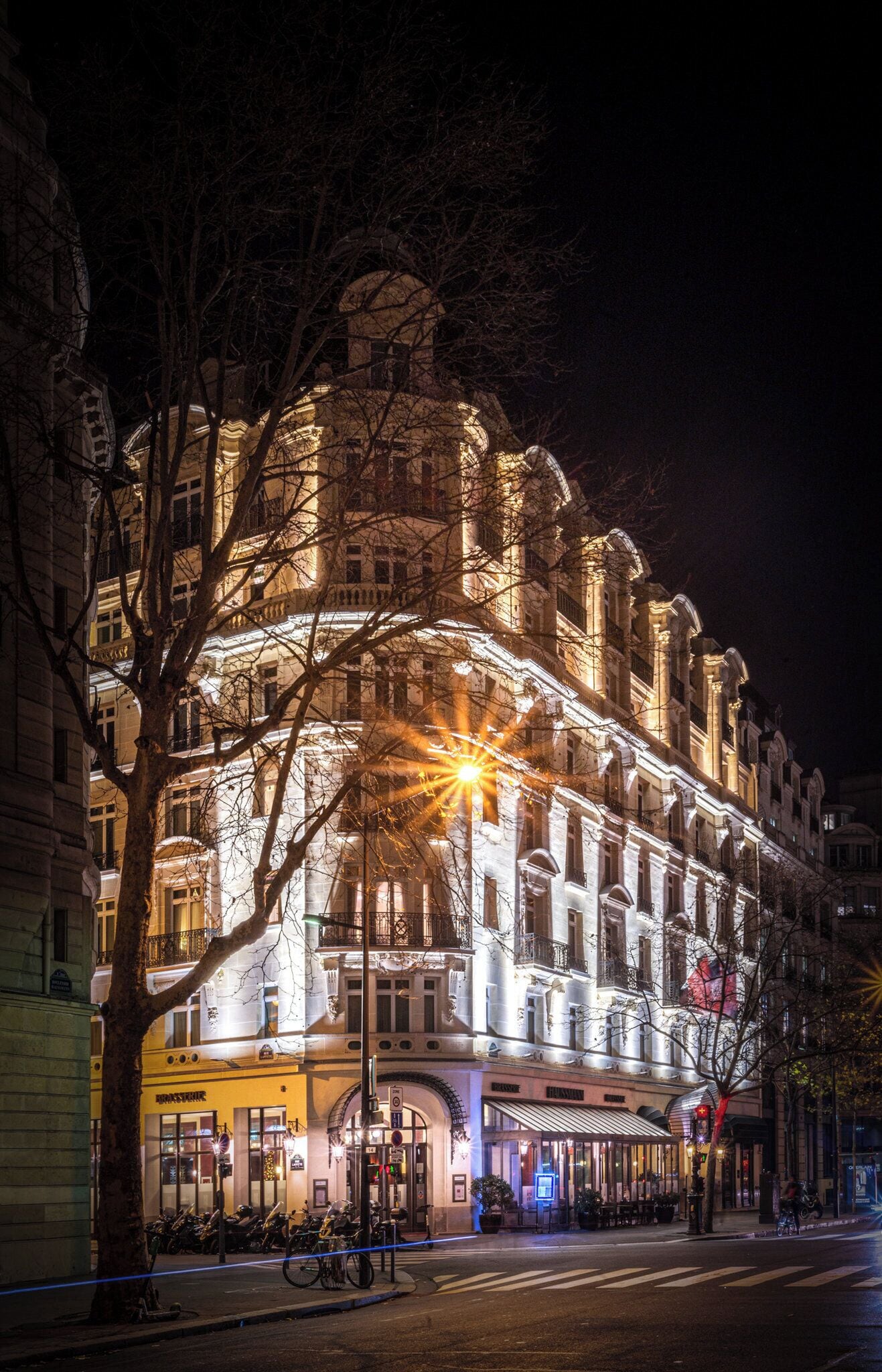 A historic building with ornate architecture, illuminated by warm lighting, and a street in front with parked bicycles.