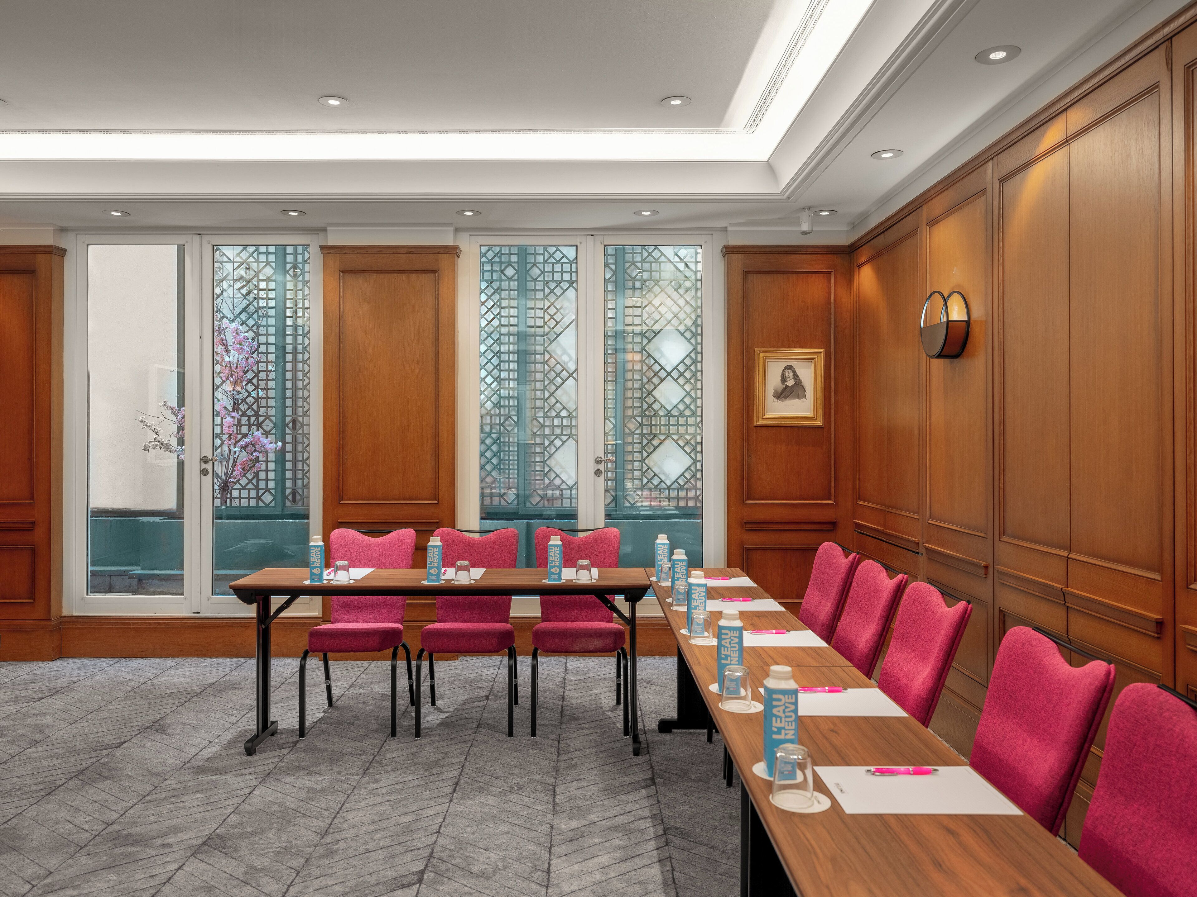 A conference room with a long table, multiple chairs, and a large window with decorative glass panels.