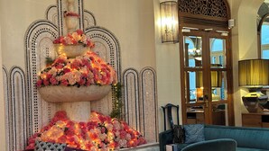 A lobby with a tiered floral centerpiece, a purple sofa, a teal armchair, and a wooden door with a mirror. - M Social Hotel Paris (Paris)