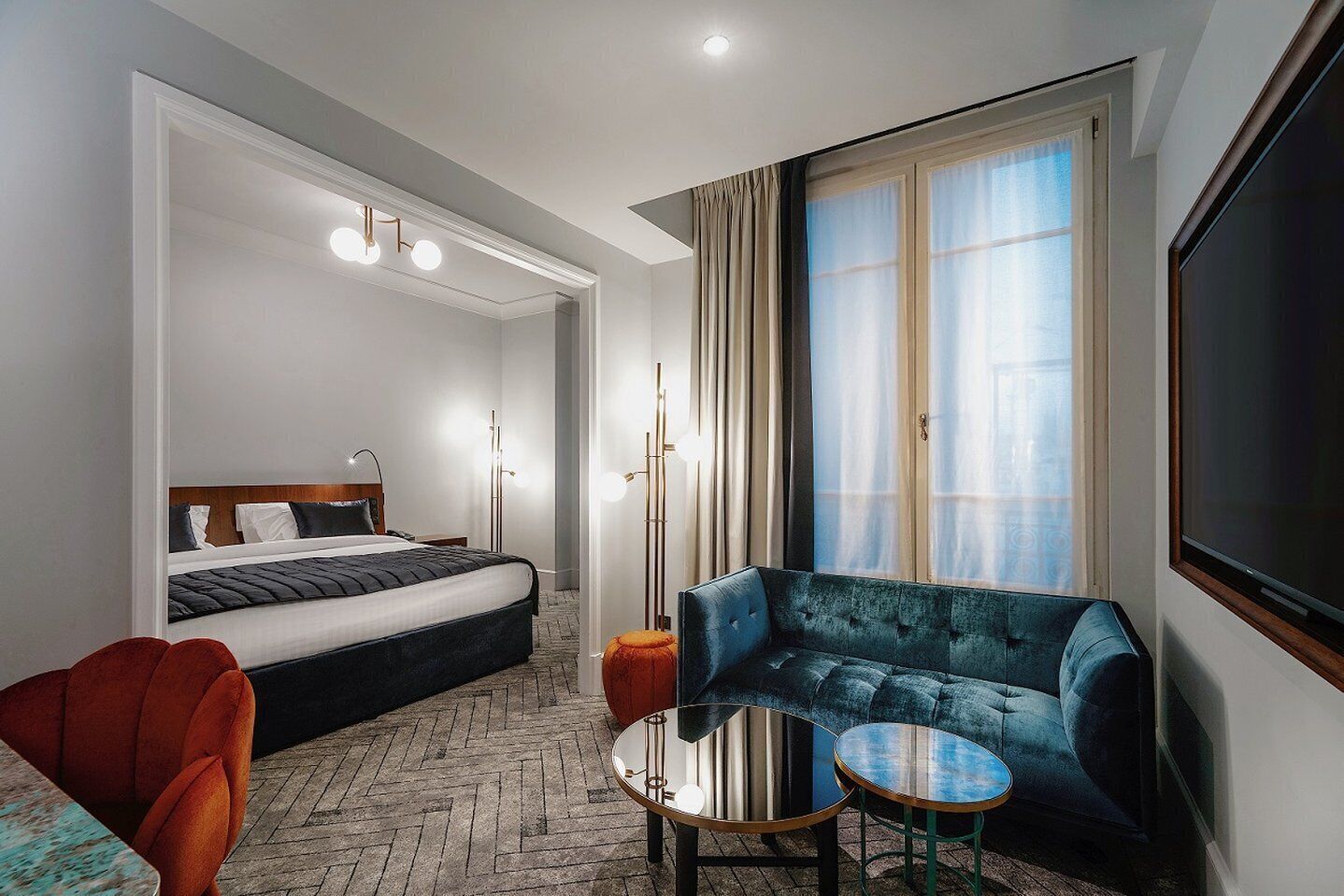 Quarto de hotel com uma cama, um sofá, uma mesinha e uma televisão.