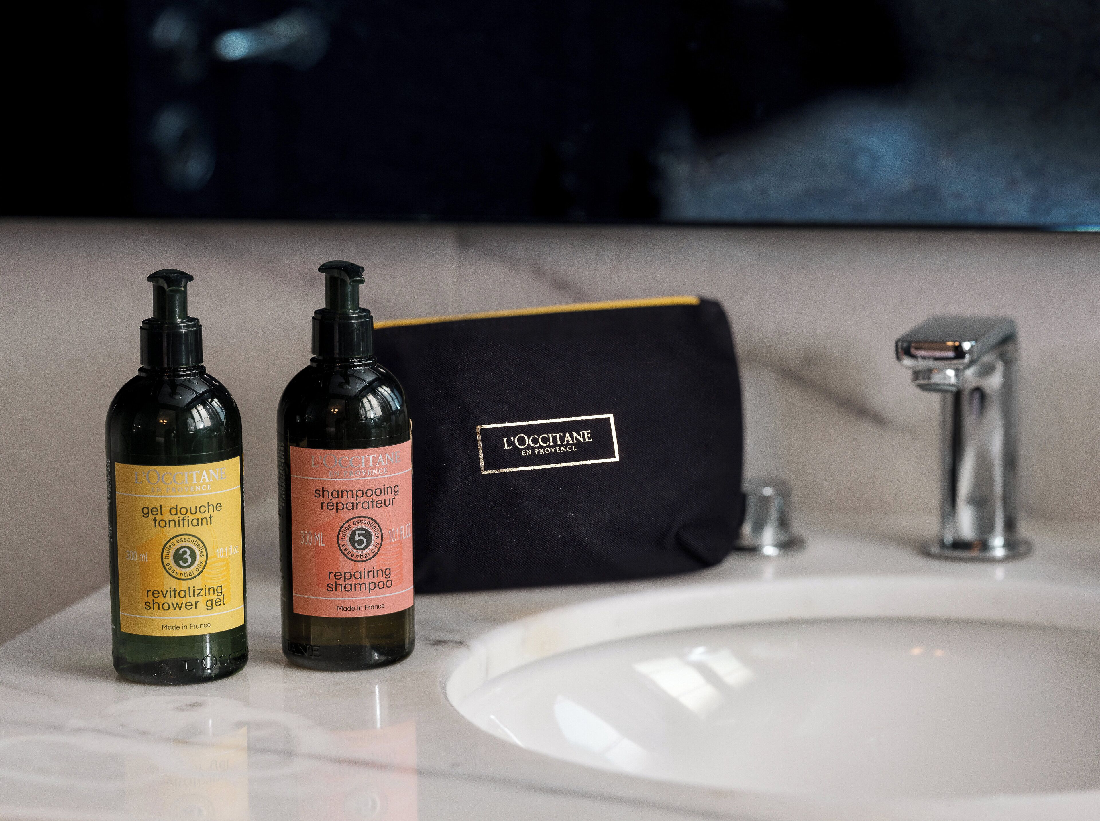 Deux flacons de produits de soins capillaires de la marque L’OCCITANE et une boîte noire sur le comptoir d’une salle de bain.