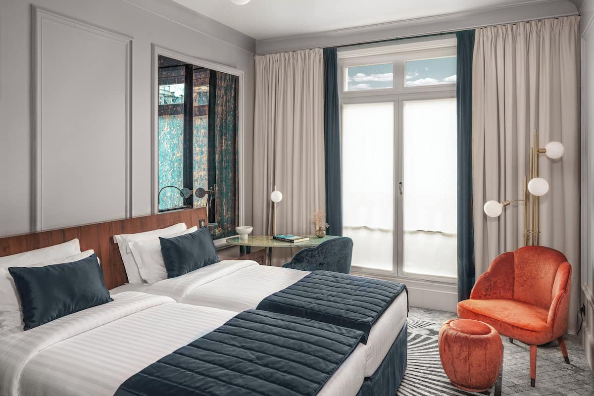 A hotel room with a large bed, a chair, a small table, and a view of the outdoors.