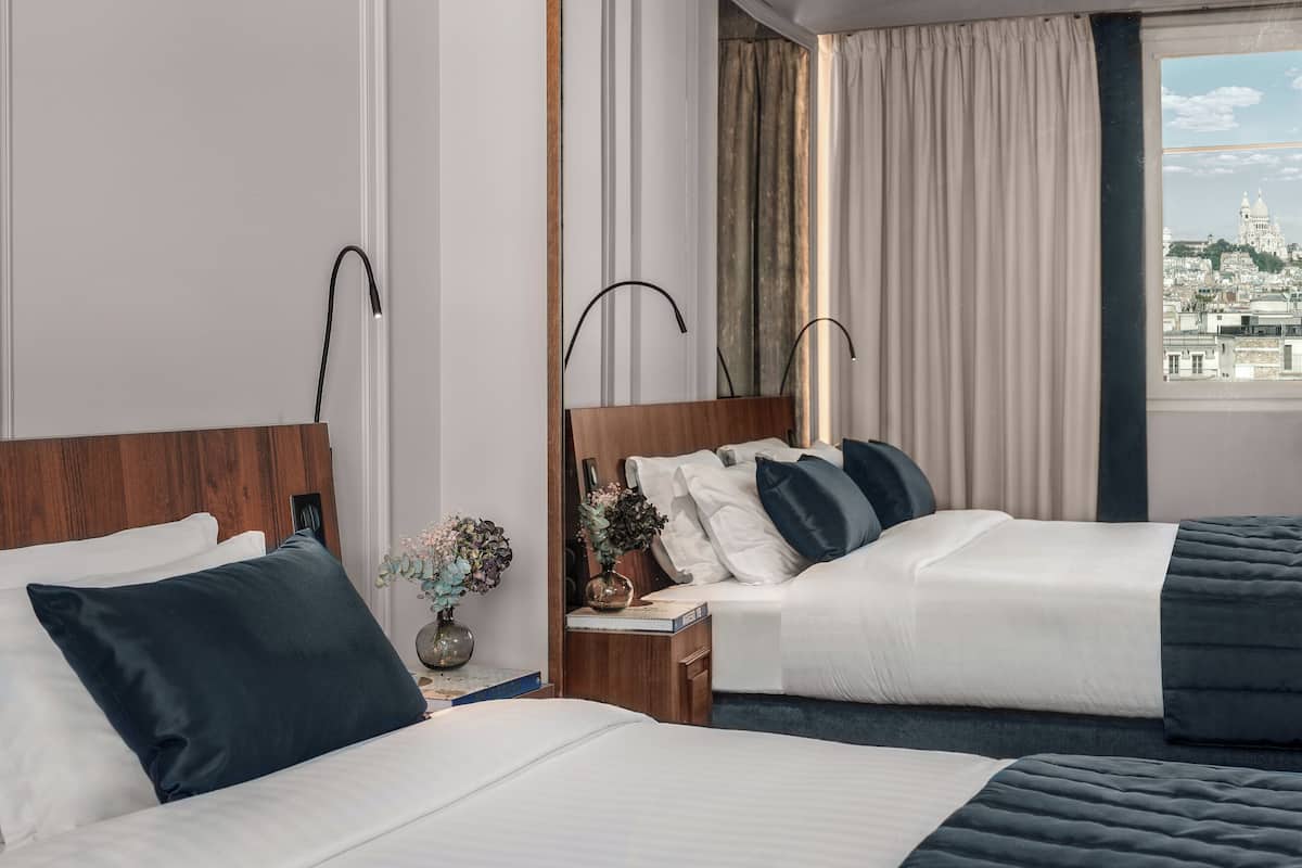 A hotel room with two beds, a view of a cityscape, and a nightstand with a vase of flowers.