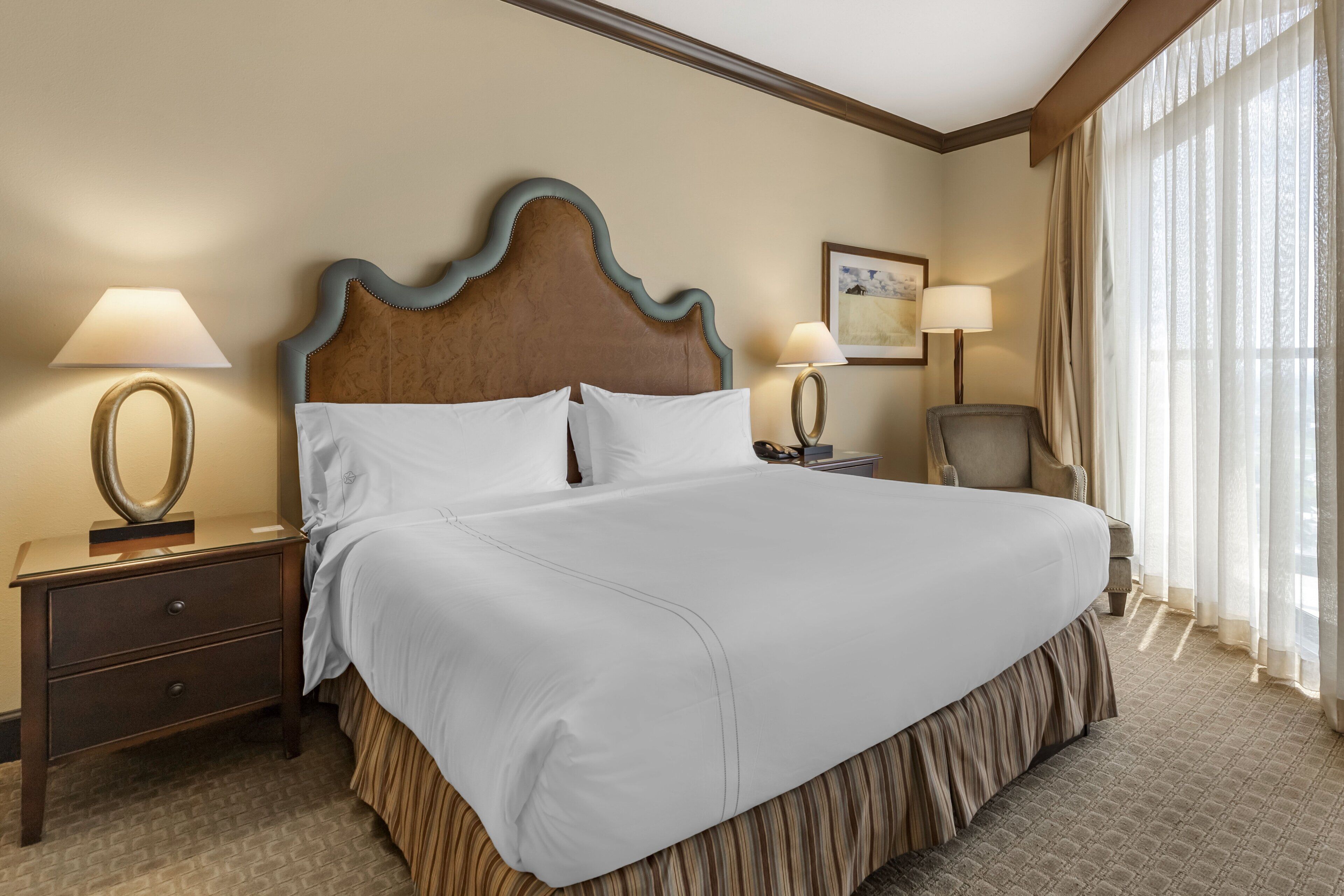 A hotel room with a large bed, two bedside tables, a chair, and a window with curtains.