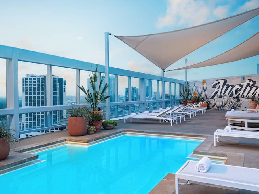 A rooftop pool area with lounge chairs, potted plants, and a large "Austin" mural.