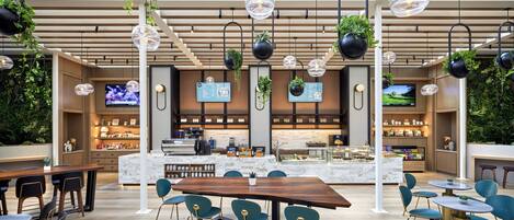 A modern cafe with a wooden ceiling, hanging plants, and a bar area with a TV screen.