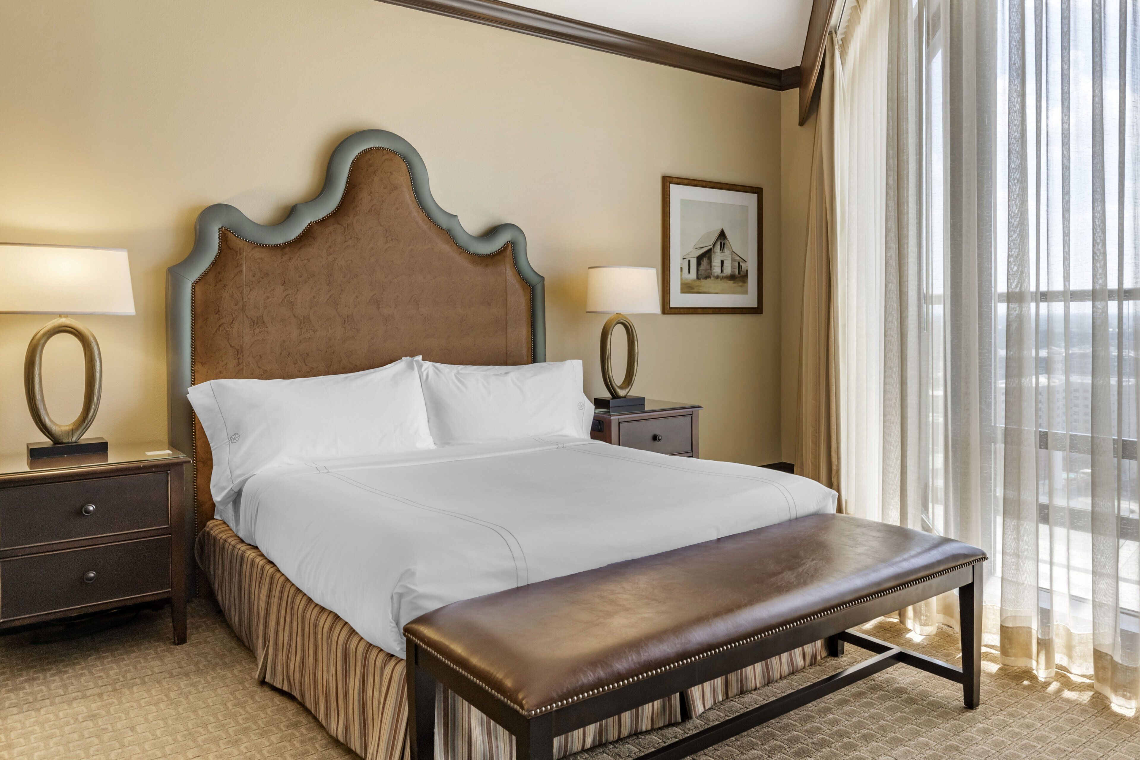 A neatly made bed with a wooden headboard, a bedside table with a lamp, and a bench at the foot of the bed.