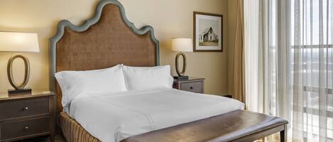 A neatly made bed with a wooden headboard, a bedside table with a lamp, and a bench at the foot of the bed.