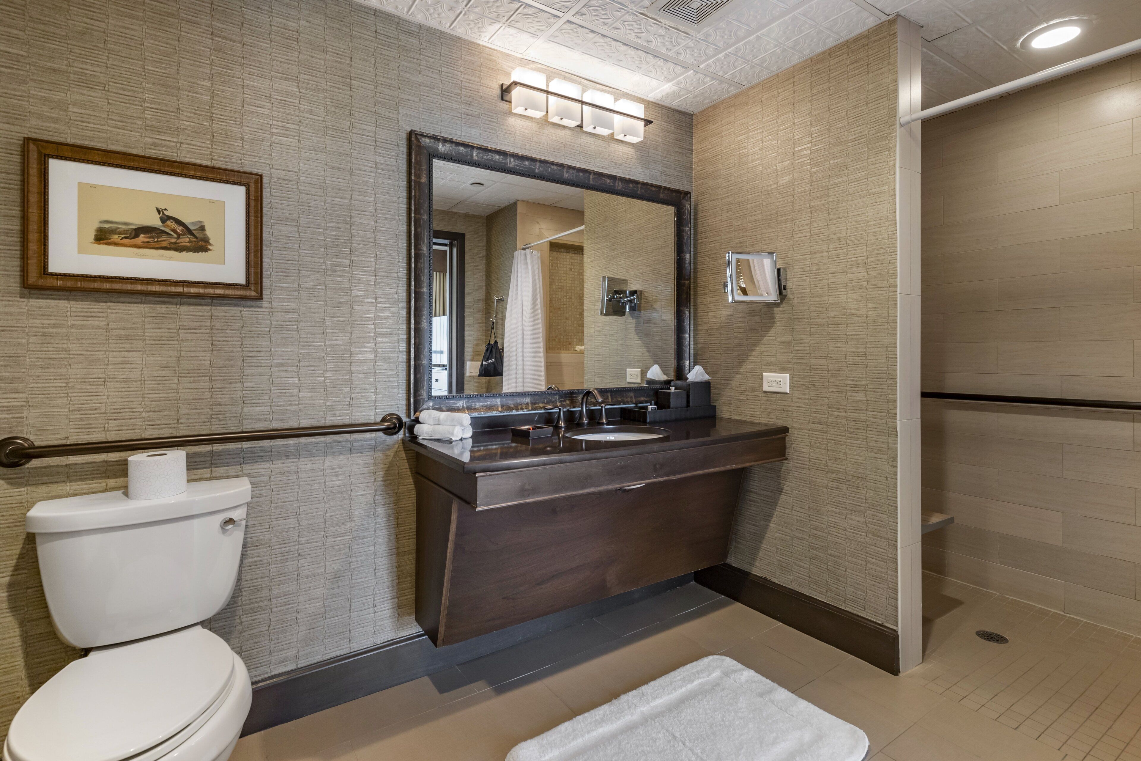 A modern bathroom with a dark wood vanity, a large mirror, and a framed picture on the wall.