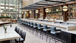 A modern bar area with high ceilings, bar stools, and a long counter. - Omni Austin Hotel (Austin)
