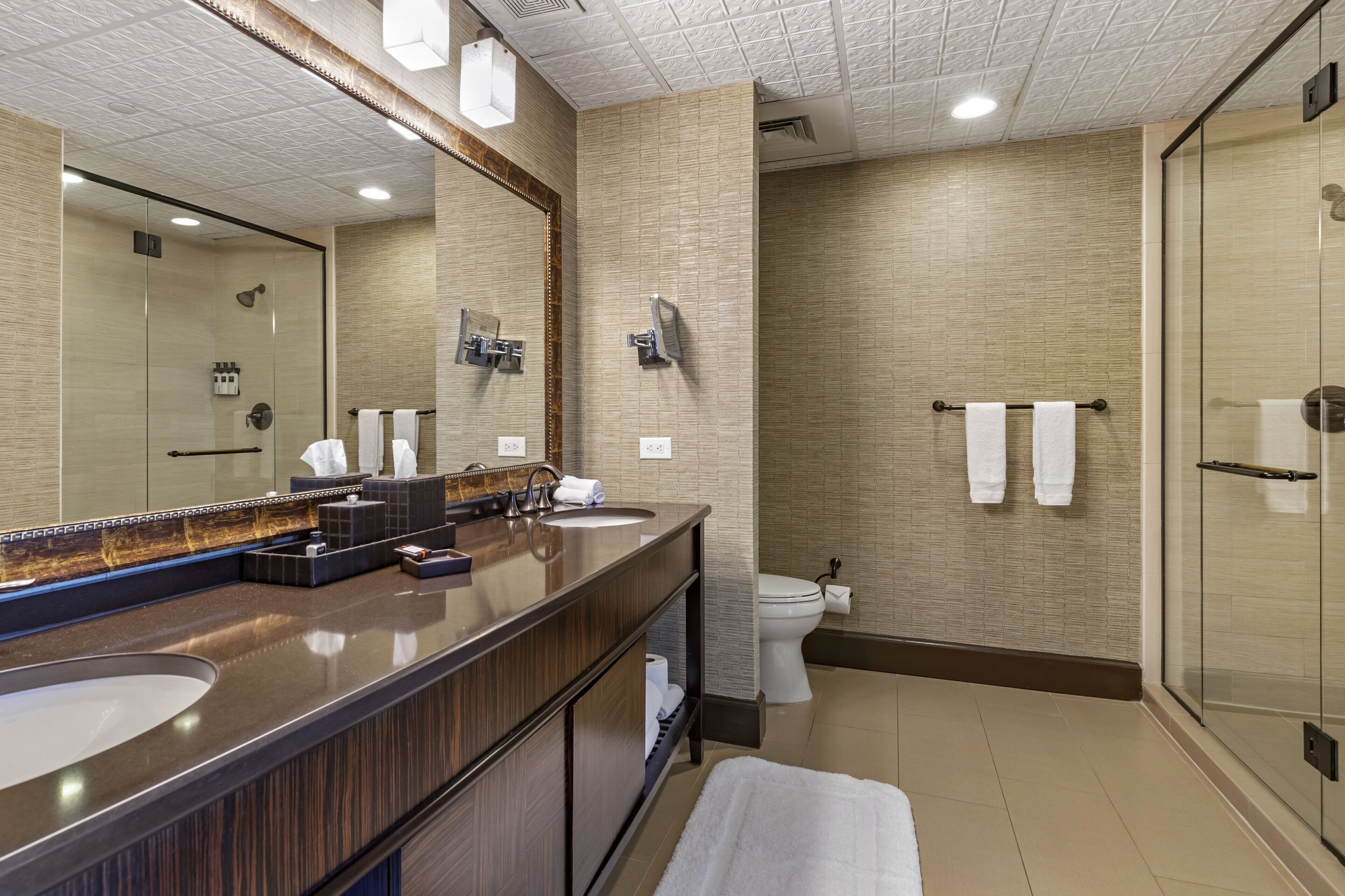 Une salle de bain moderne avec un grand miroir, un lavabo, des toilettes et une douche à parois de verre.