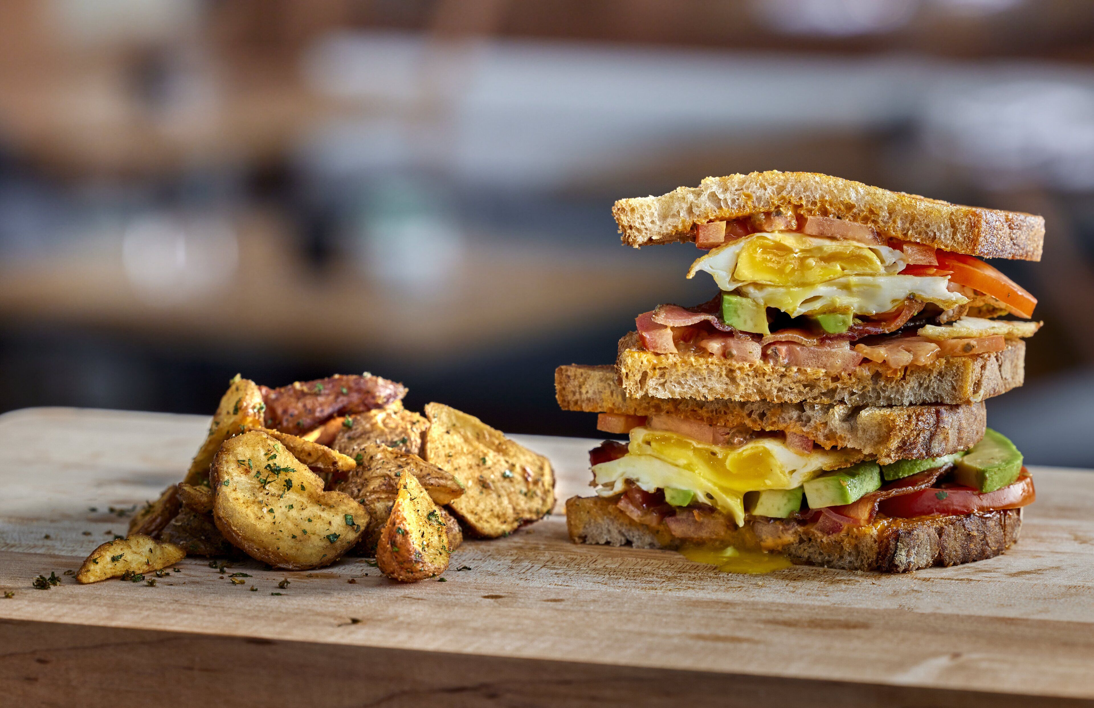 A sandwich with various ingredients and a pile of roasted potatoes on a wooden surface.