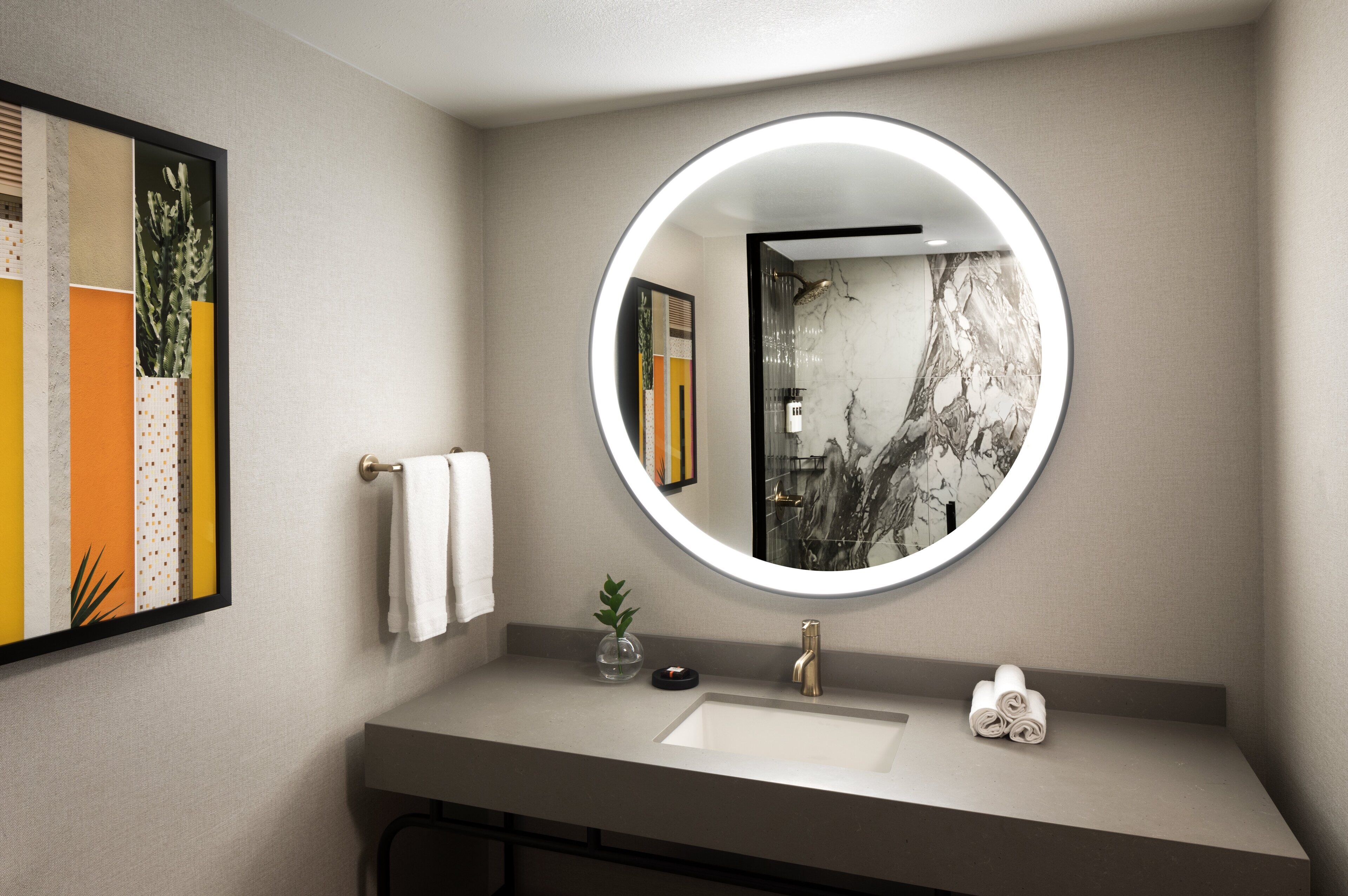 Un baño moderno con un espejo redondo, un lavabo blanco y un perchero para toallas.