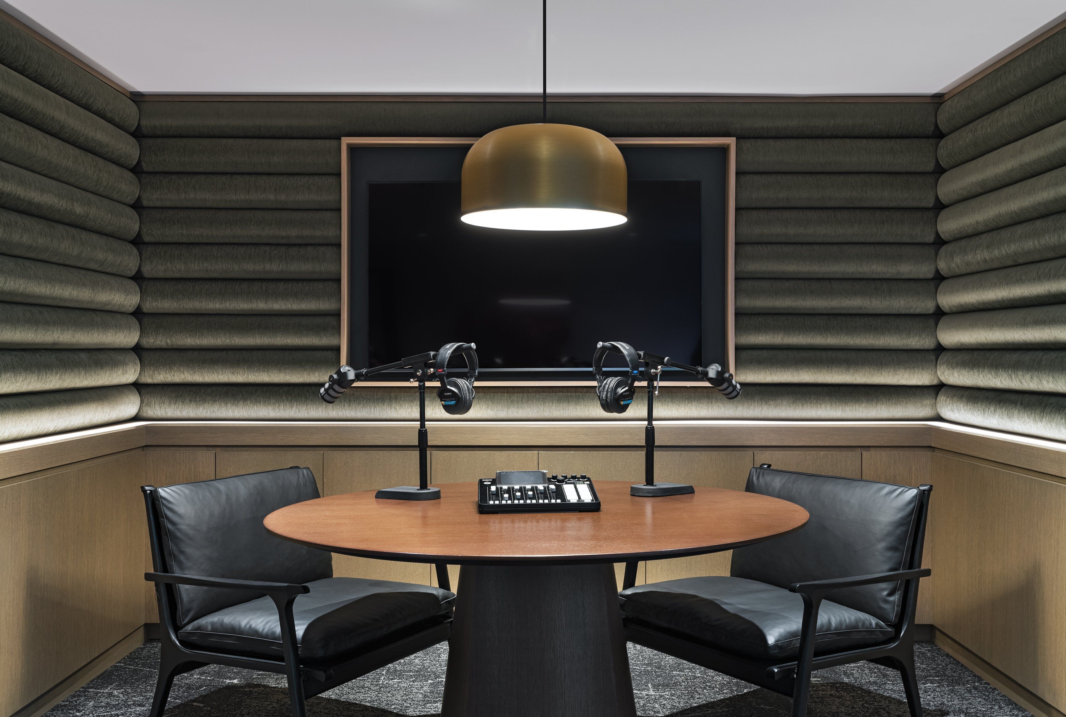 A conference room with a round table, two chairs, a sound mixer, and a large window with soundproofing panels.