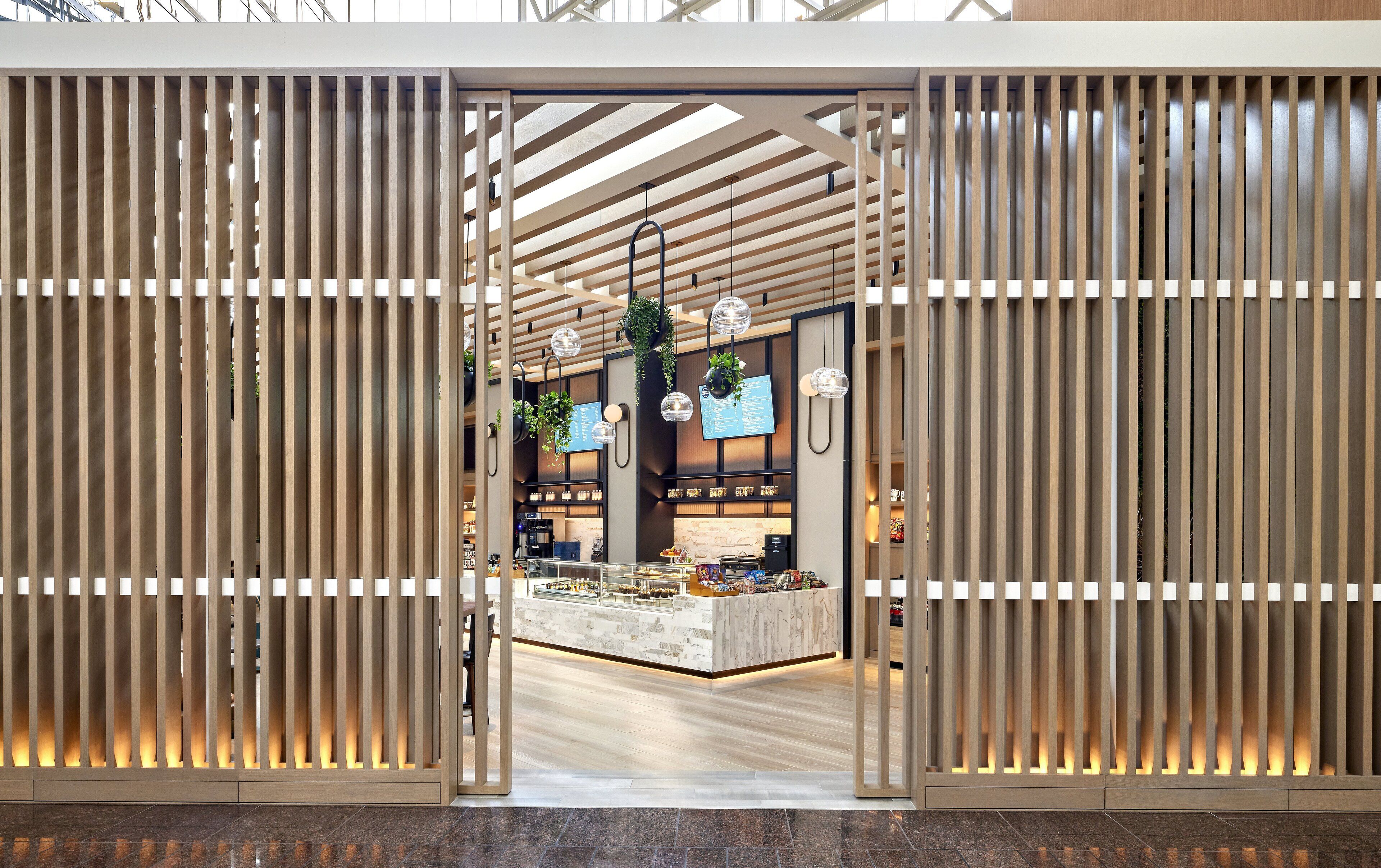 A modern interior with a central counter, hanging plants, and a wooden slatted entrance.