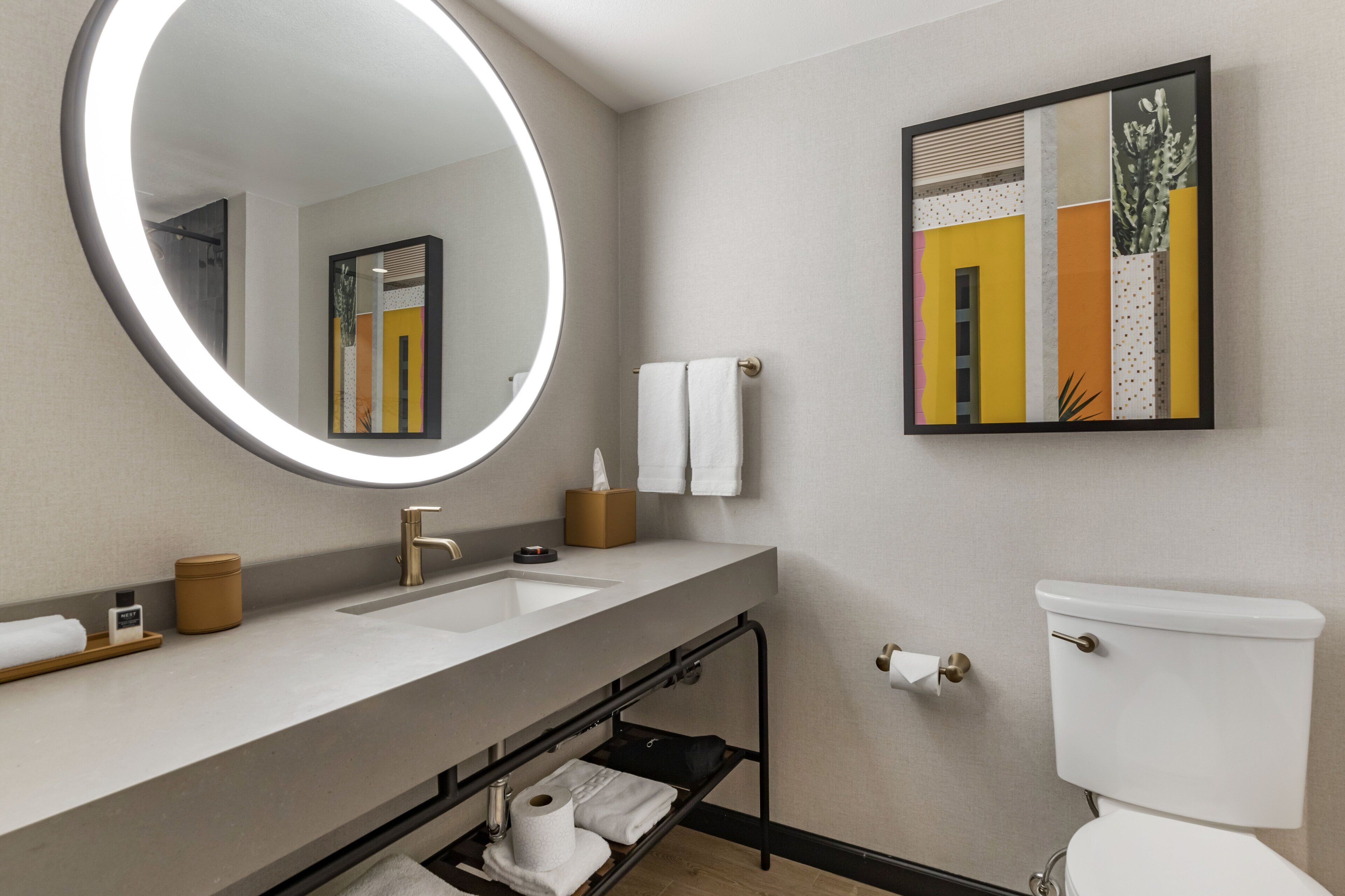Un baño moderno con un espejo grande, dos lavamanos, un inodoro y una obra de arte enmarcada en la pared.
