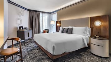A hotel room with a large bed, a desk with a chair, a nightstand, a lamp, and a wall-mounted artwork.
